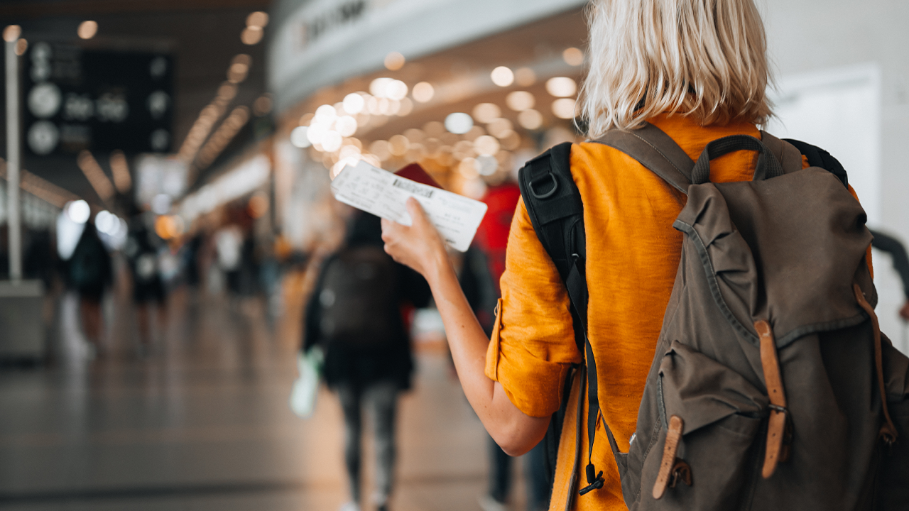 Rear view of a woman at the airport holding a passport with a boarding pass as she walks to her departure gate