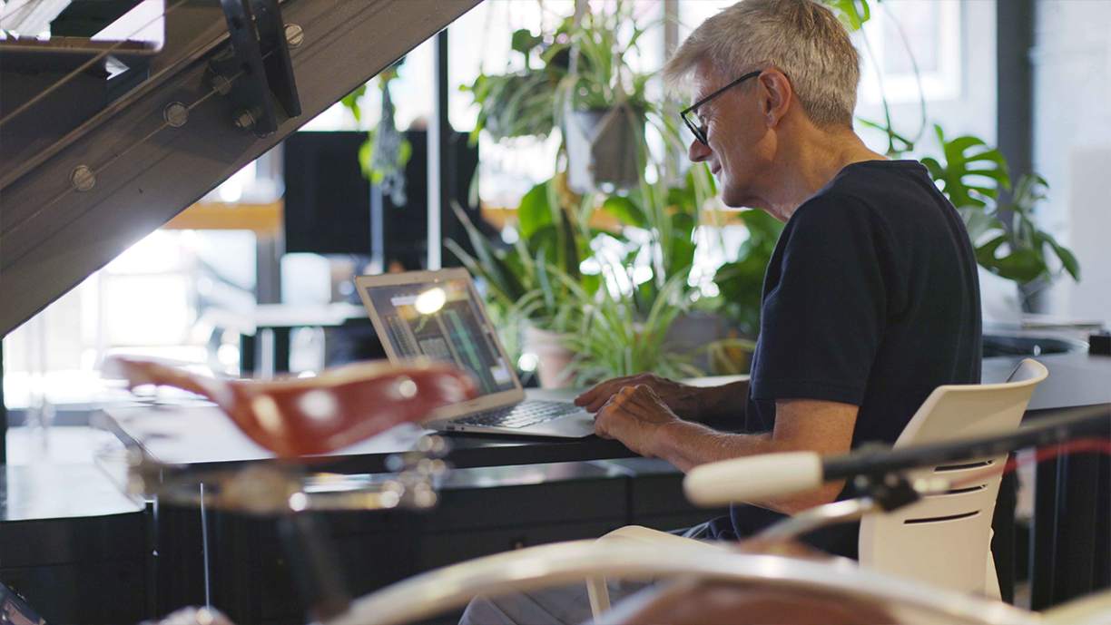 Sustainability reporting update image. Mature man’s hands working at a laptop on an office desk full of house plants