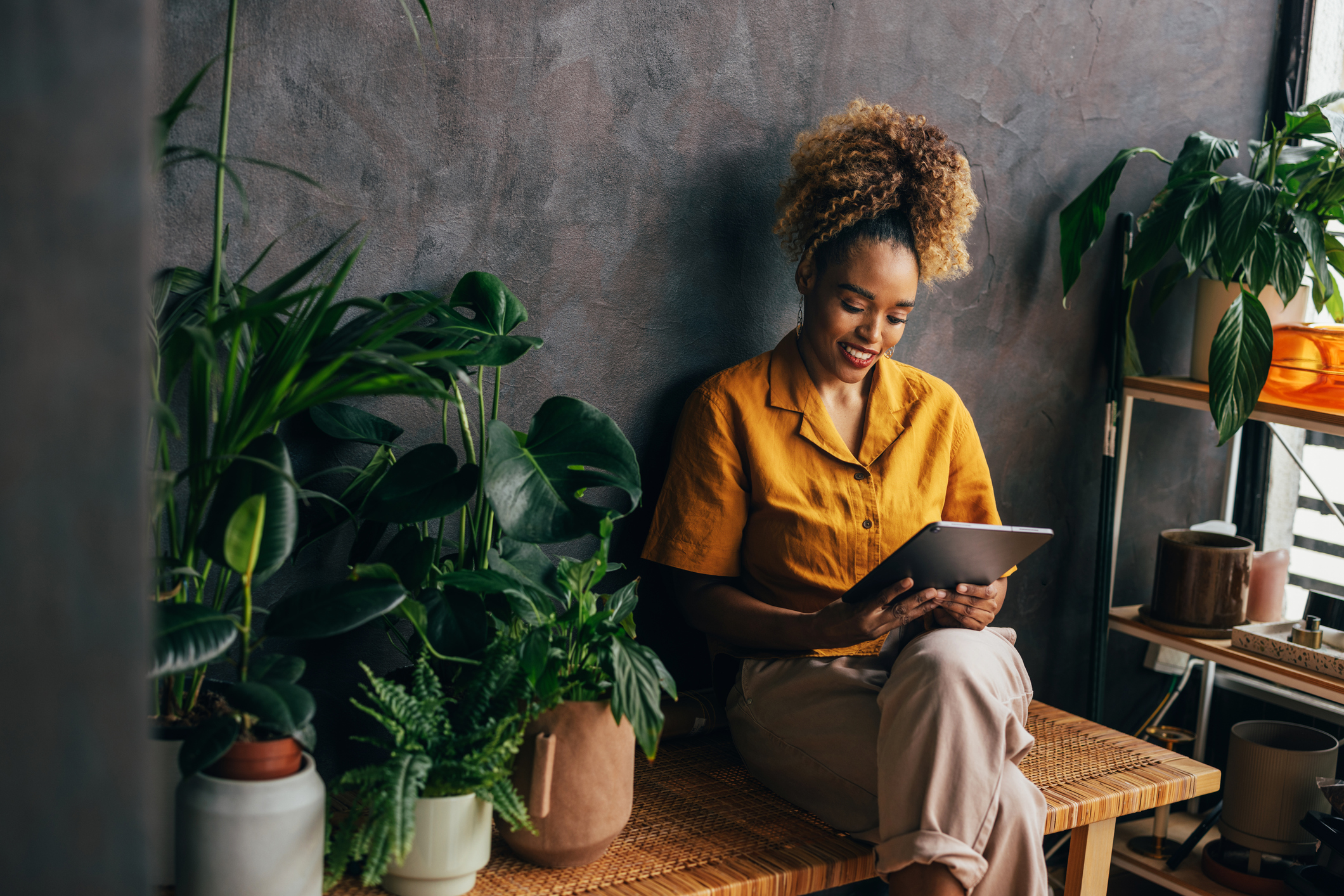 A Happy Beautiful Blonde Businesswoman Using Her Tablet While Sitting Indoors Surrounded By Her Houseplants