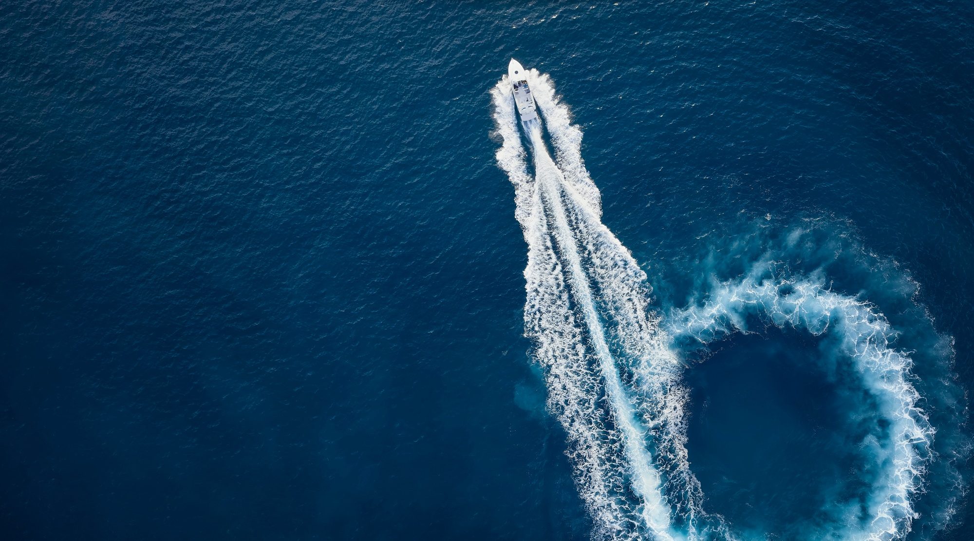 Aerial top view of a motor powerboat forming a circle of waves and bubbles with its engines over the blue sea